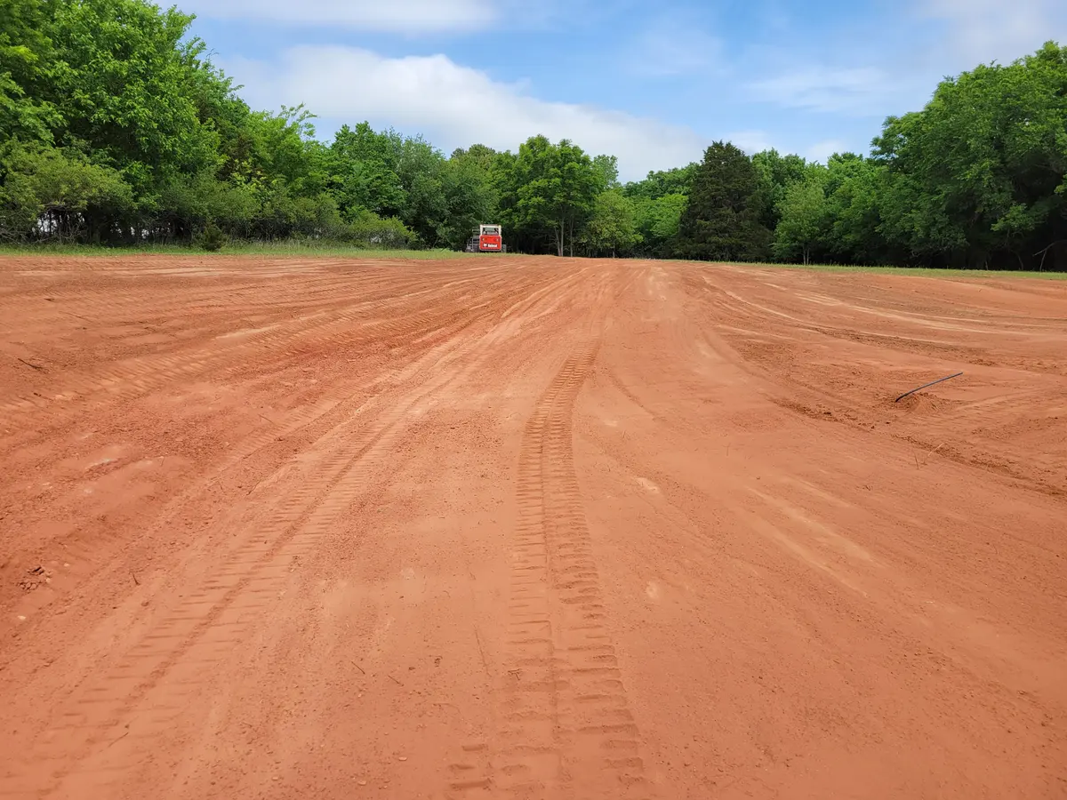 Expansive freshly graded red dirt pad with a skid steer working in the distance