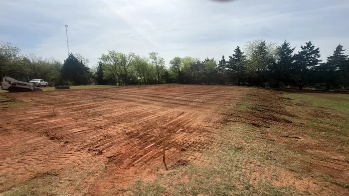 Wide acreage lot regraded to red dirt between grass edges and a cedar windbreak