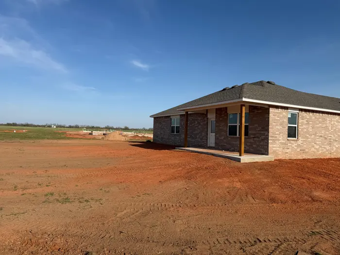 Red dirt yard grade wrapping a new brick home on open acreage
