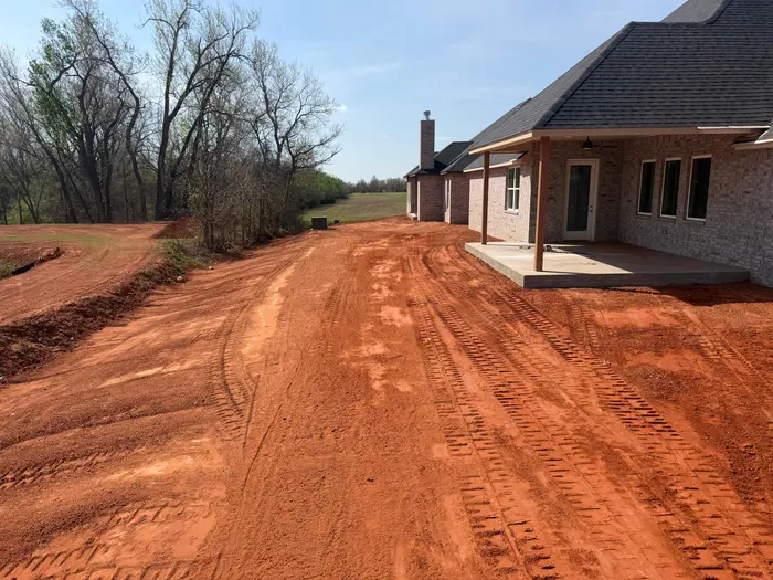 Backyard regraded in red dirt along the covered patio of a new brick home