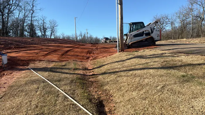 Track loader cutting a red dirt driveway approach in golden light
