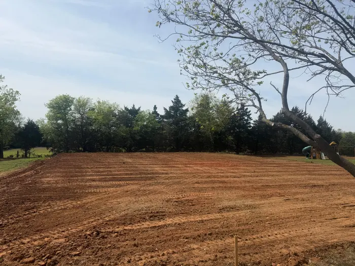 Field final graded in even red dirt passes, tree line at the back