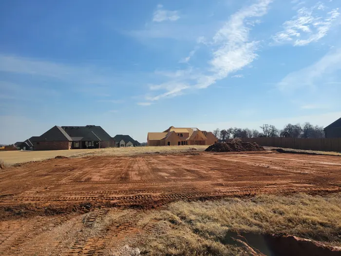 Freshly graded red dirt homesite pad in a new addition, framing underway behind