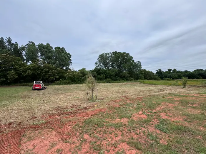The same pasture brush hogged to clean grass, skid steer finishing the far strip