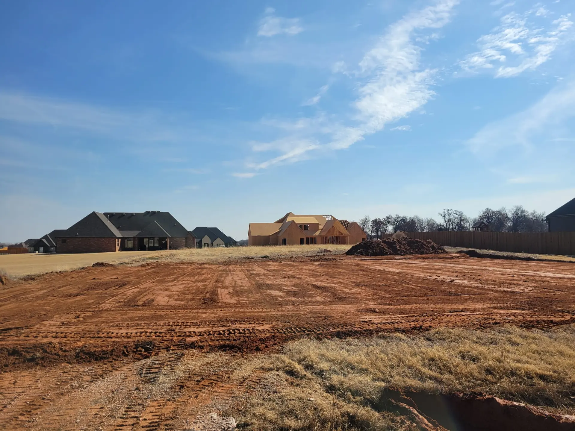 Freshly graded red dirt homesite pad in a new addition, houses going up behind it