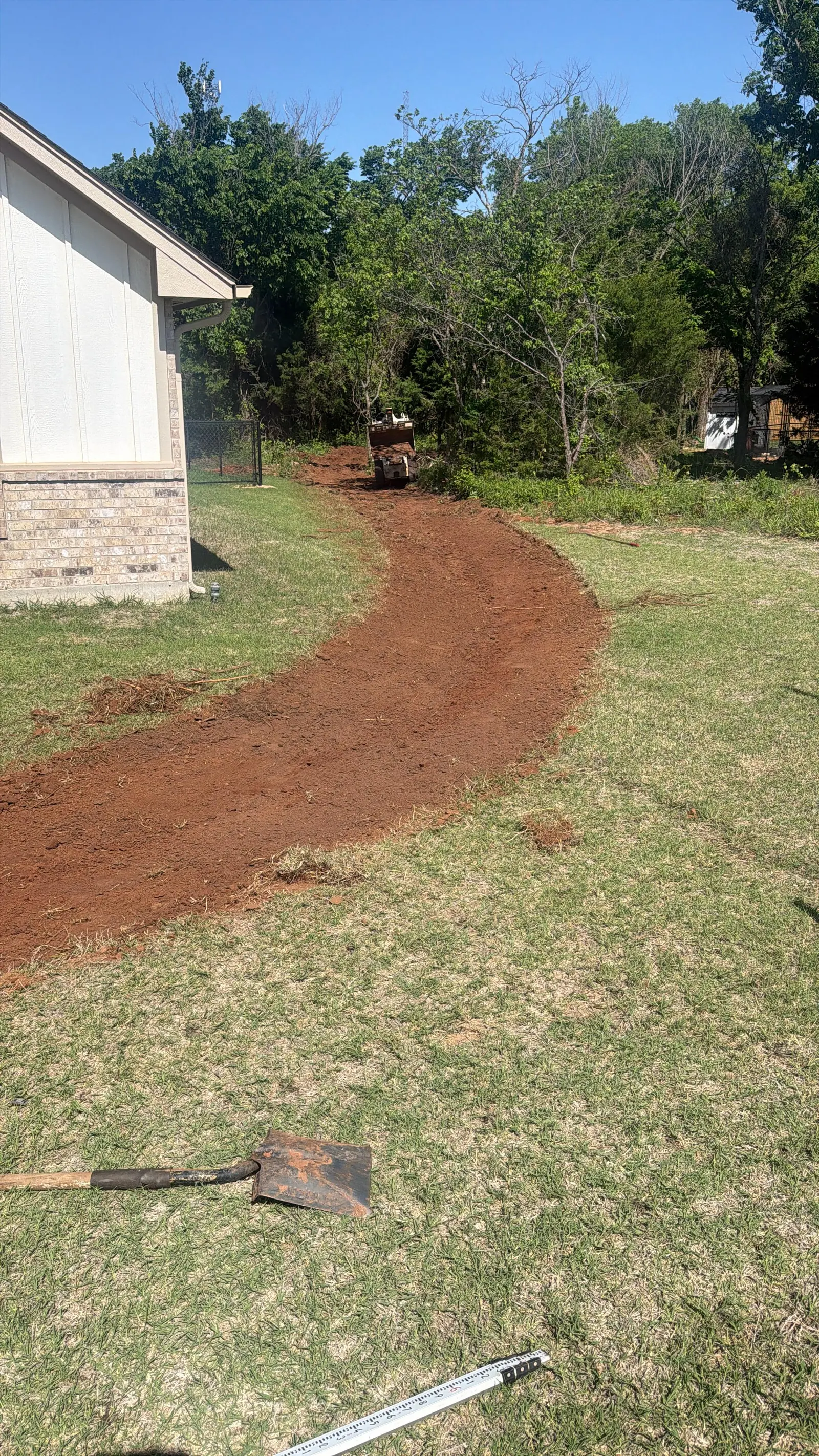 Drainage swale cut curving through a lawn with a compact roller working at the far end